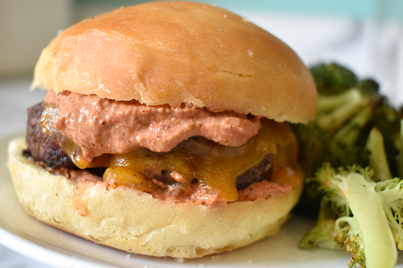 A burger topped with melted cheddar cheese and burger sauce on a plate