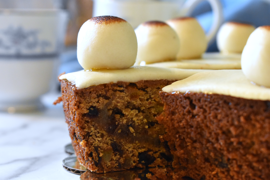 A slice of simnel cake, topped with a marzipan ball, coming out of the full cake